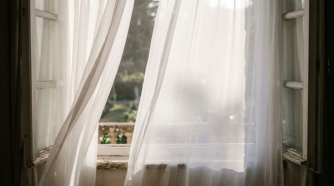 Sheer white curtains billowing at an open window with soft daylight and a garden beyond